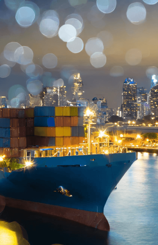 A cargo ship docked at a harbor at night illuminated by onboard lights.